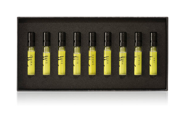 The AKRO 9 x 2ml Discovery Kit by Akro features nine perfume sample vials, labeled: HAZE, DARK, BAR, RISE, SMOKE, HALF, MALT, NIGHT, and INK. These indulgent scents are arranged neatly in a black rectangular box.