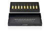 An open black box from the AKRO 9 x 2ml Discovery Kit by Akro reveals a collection of nine small vials filled with yellow liquid, neatly organized in a foam insert. The lid of the box features various words such as "passion," "chocolate," and "caffeine." These bold fragrances turn addictions into perfumes, promising an enticing olfactory experience.