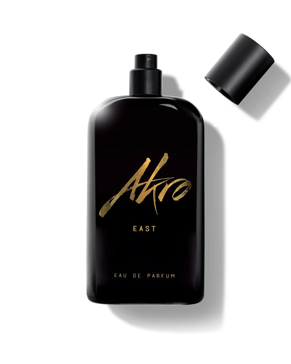 A black perfume bottle labeled "East" by Akro evokes the essence of Oud from the Middle East, with "Eau de Parfum" inscribed at the bottom. The cap is off and placed to the right.