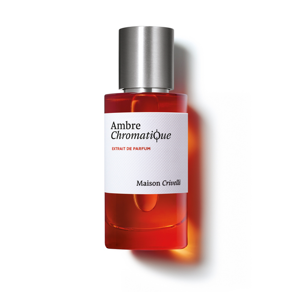 A bottle of Ambre Chromatique by Maison Crivelli, showcasing red liquid, a white label, and a silver cap, highlights an amber accord that adds depth to this exquisite extrait de parfum.