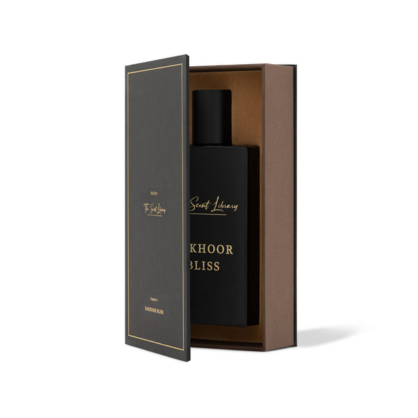 A black perfume bottle labeled "Bakhoor Bliss" is partially revealed from an open black and brown box with gold writing, evoking a sense of spiritual tranquility akin to the calming scent of The Scent Library.
