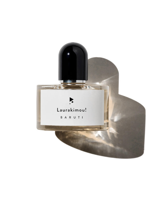 A perfume bottle labeled "Laurakimoui! Baruti" with a black cap is centered on a white background, casting a shadow below. This unisex fragrance boasts hints of leather and magnolia overdose, making it captivating for all.