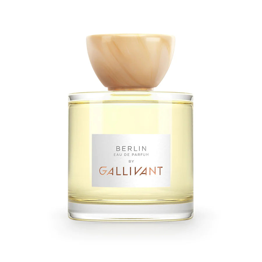 A bottle of Berlin by Gallivant by Gallivant Perfumes. It has a light-colored liquid inside, a label on the front, and a round wooden cap. This Berlin-inspired fragrance features woody citrus spicy perfume notes of grapefruit, clementine, and lemon.