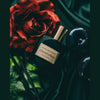 A bottle of Danse Sauvage by Chris Collins sits on a black satin surface, exuding a sensual scent, accompanied by a red rose and dark decorative elements.