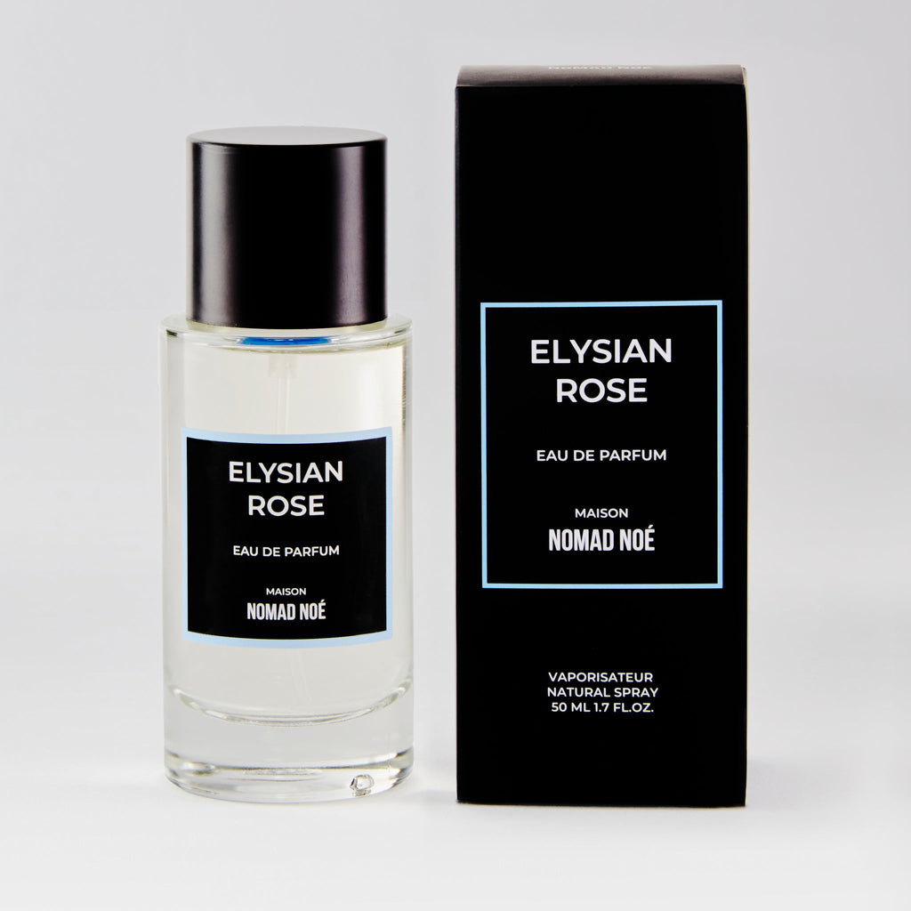 A bottle and box of Nomad Noe Elysian Rose Eau de Parfum. The bottle is transparent with a black label and cap, while the box is black with white text. This floral fragrance captures the essence of a modern rose scent, perfect for any occasion.