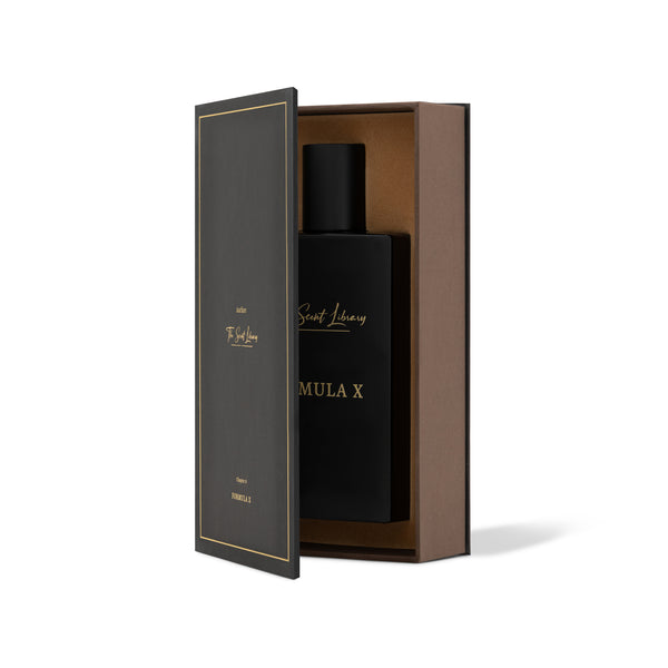 A black perfume bottle labeled "FORMULA X" from The Scent Library sits partially inside an open black and brown rectangular box with gold trim and text, revealing its alchemist's secret: an enchanting iris fragrance.