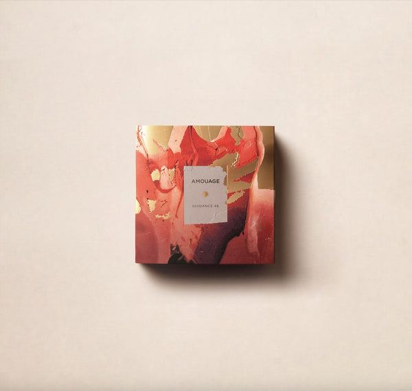 A square box of Amouage Guidance 46, featuring an abstract design in warm shades of red, gold, and pink, placed against a plain, light-colored background. This exquisite perfumery item stands out with its exceptional 46% concentration.