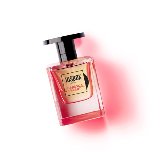 A bottle of Jusbox with "Carioca Heart" label, created by the renowned perfumer Julien Rasquinet. The pink perfume bottle, accented with a black cap, sits on a white background with a pink tint to the left. This scent encapsulates the essence of Fruity Woody Musky notes blending effortlessly like a Bossa Nova melody.