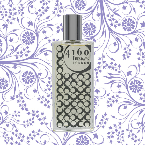 A bottle of 4160Tuesdays Hush Hush perfume featuring a circle-patterned label, set against a floral and leaf-patterned background with purple hues, exuding hints of Cashmeran.