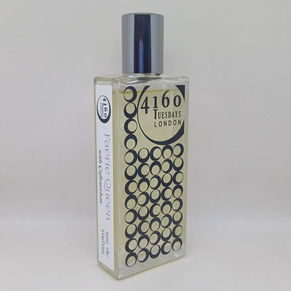A clear rectangular perfume bottle with a silver cap and a label reading "4160Tuesdays" and "Faerie Queen." The design includes a pattern of black circles. Experience the enchanting blend of lipstick fragrance with hints of vanilla and kumquat.