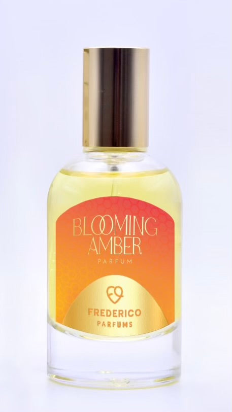 A bottle of Frederico Parfums’ Blooming Amber with a gold cap and an orange-yellow gradient label, known for its long-lasting scent.