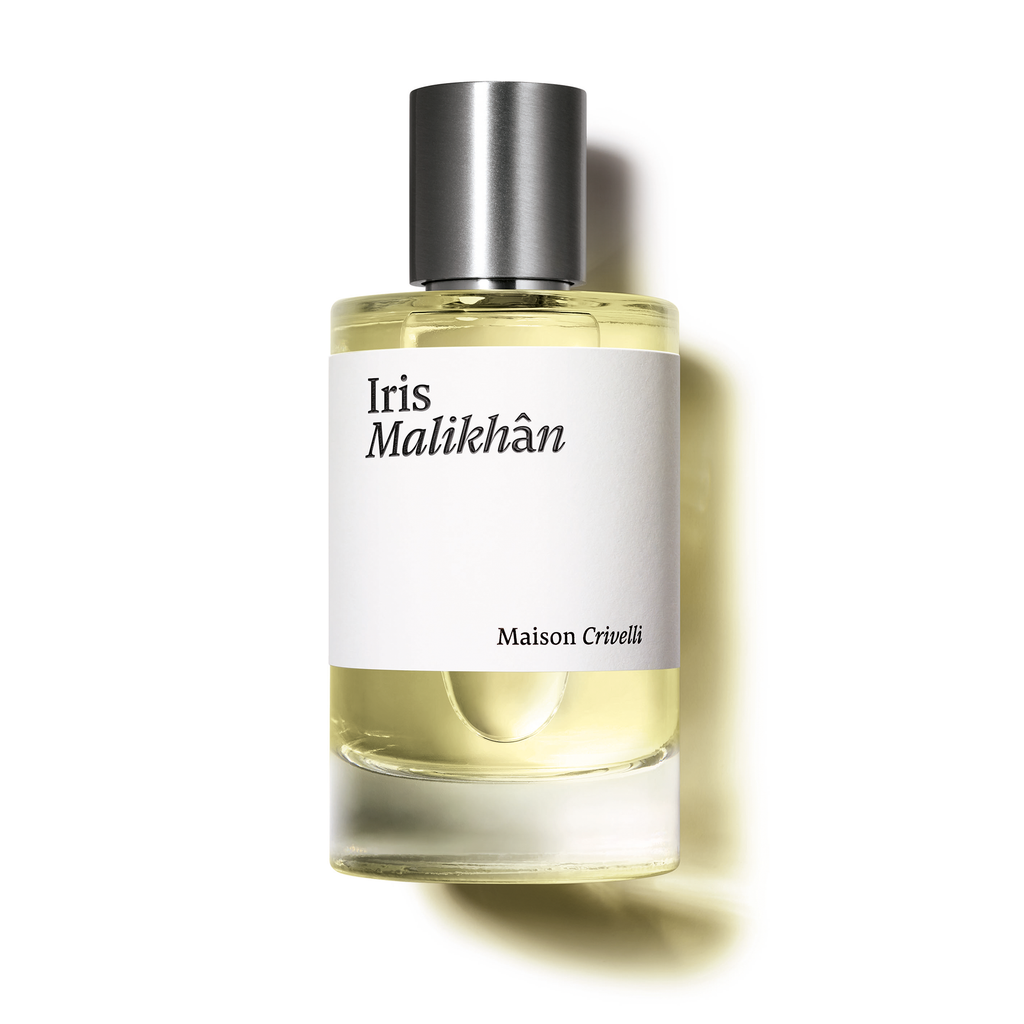 A clear glass bottle of Maison Crivelli's Iris Malikhân perfume with a metallic cap, containing a light yellow liquid, exudes an addictive accord with hints of powdery gourmand leather.