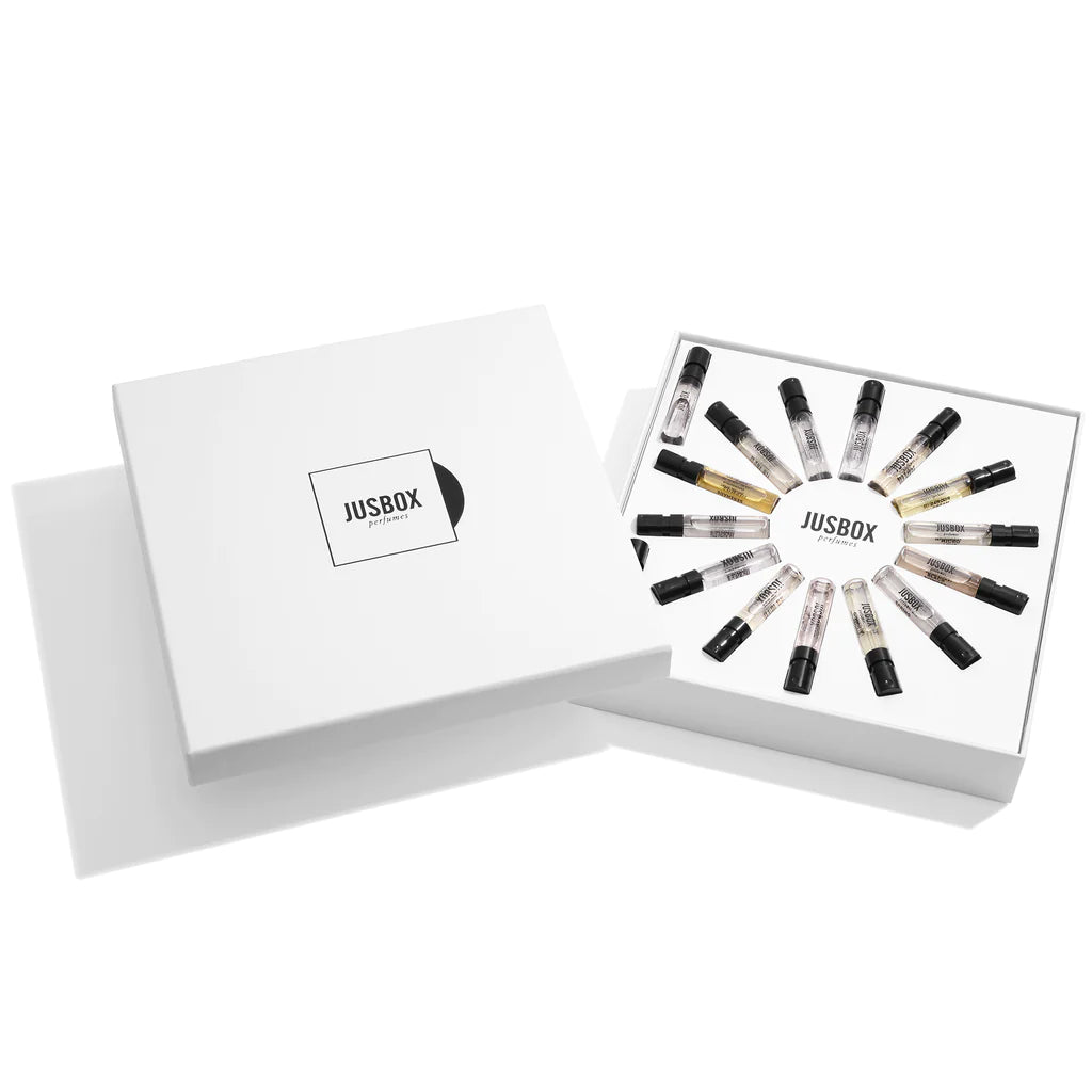 A white box titled "Jusbox" contains 13 small, transparent sample vials arranged in a circular pattern, each with a black cap and visible contents. The Jusbox Discovery Set 14 X 1.5ml elegantly melds the world of music and perfume.