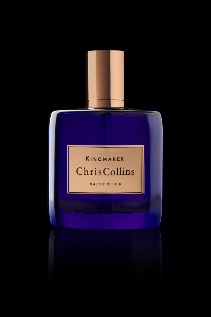 A blue glass bottle of perfume labeled "Chris Collins KINGMAKER | Master Of Oud" with a gold cap and label, featuring the richness of Pure Oud Assam, set against a black background.