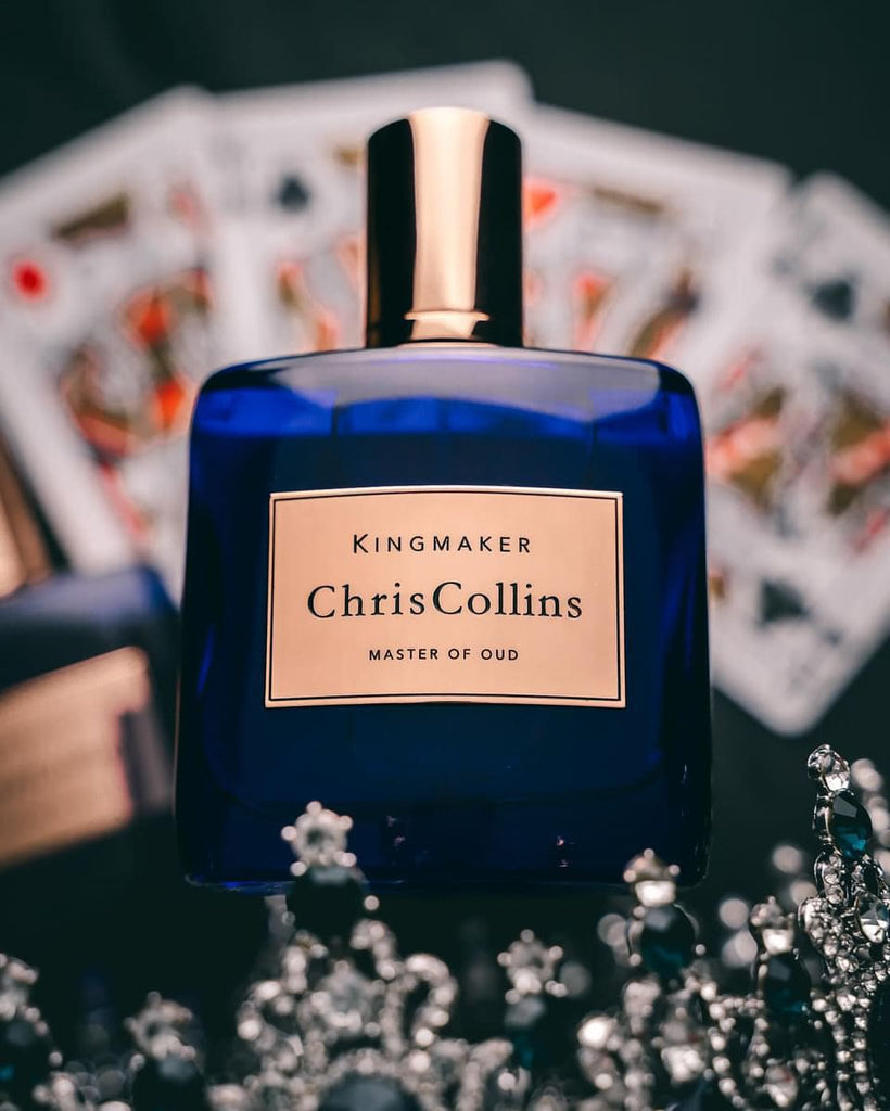 A blue bottle of Chris Collins KINGMAKER | Master Of Oud is placed in front of a fan arrangement of playing cards, hinting at rich notes like Pure Oud Assam.