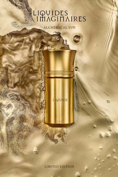 A gold bottle of Liquide Gold perfume by Liquides Imaginaires is placed on a textured, flowing gold and brown surface. Text above reads "Alchemical Sun," and below reads "Limited Edition.”
