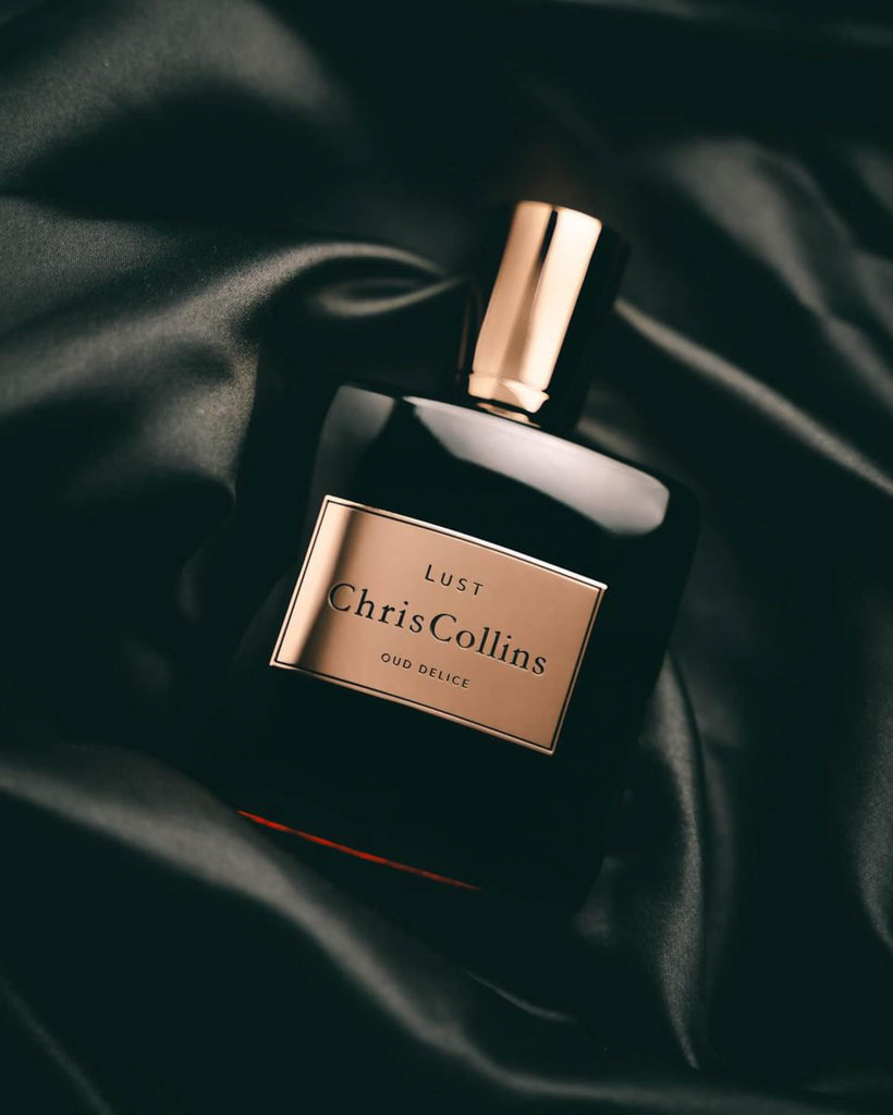 A bottle of Chris Collins LUST | Oud Delice perfume lies on a black silky fabric, exuding the allure of sensual musks.