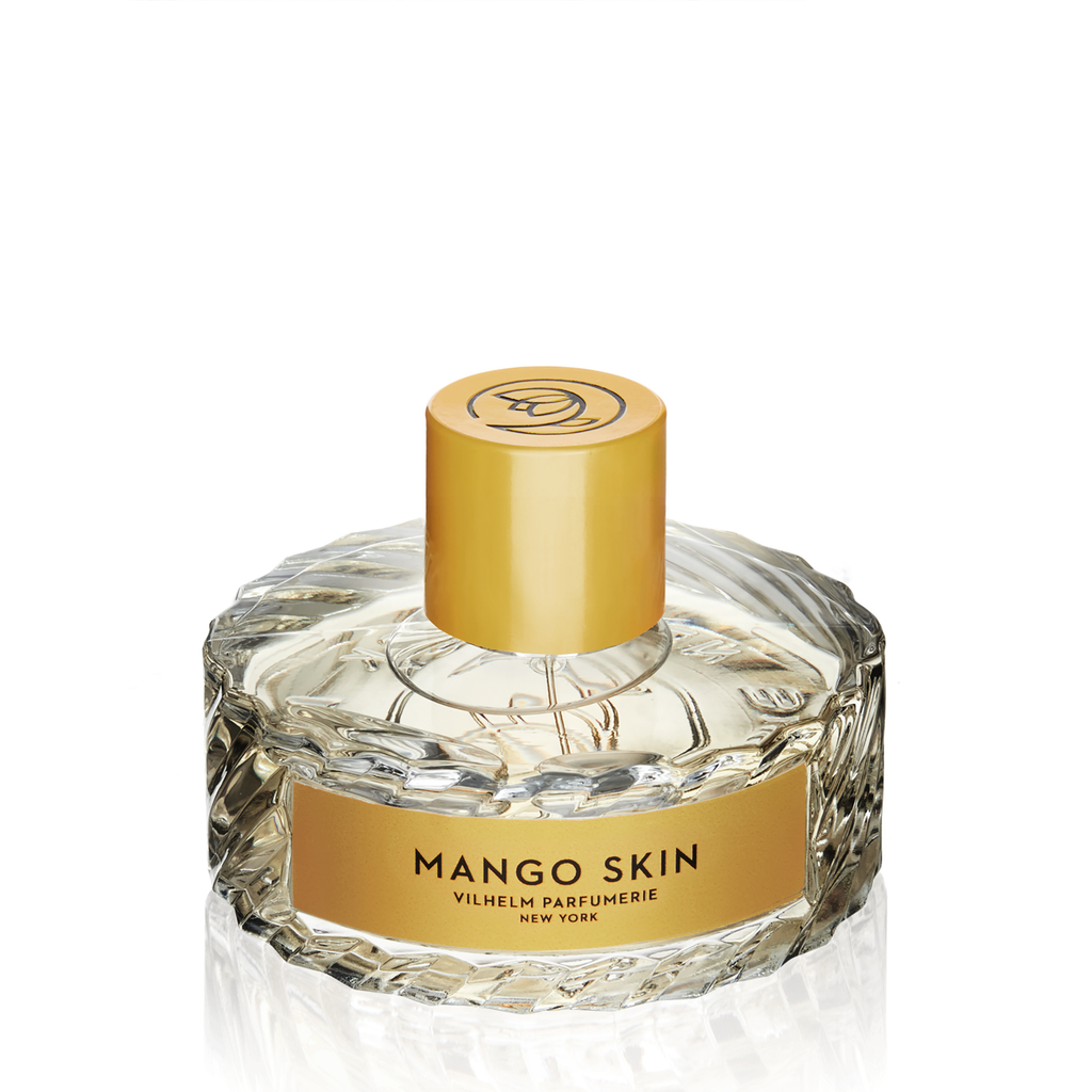A round, clear perfume bottle with a textured design and a yellow cap. The label reads "Mango Skin, Vilhelm Parfumerie, New York," hinting at the luscious notes of mango intertwined with subtle undertones of patchouli.