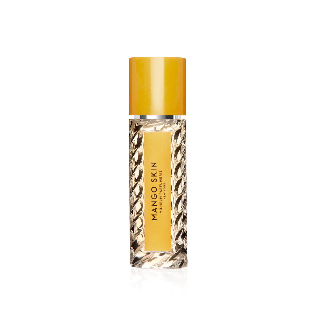 A clear glass bottle with a yellow cap and a label that reads "Mango Skin Eau de Parfum" by Vilhelm Parfumerie, exuding hints of juicy blackberries and warm patchouli.