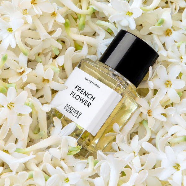 A bottle of Matiere Premiere French Flower eau de parfum with a black cap and white label lies on a bed of tuberose blossoms.