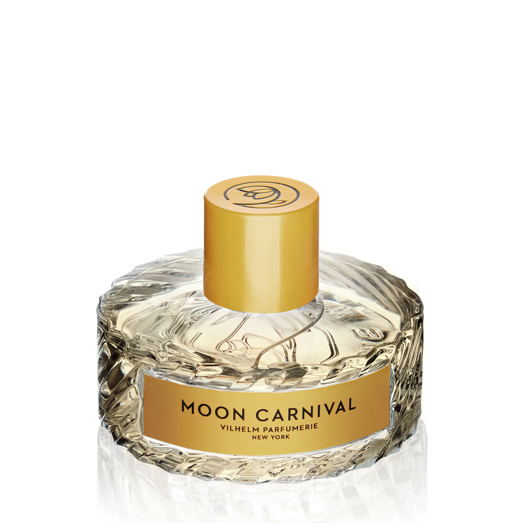 A bottle of Moon Carnival perfume by Vilhelm Parfumerie, featuring a circular, textured glass design with a gold cap. The label on the front showcases its name and brand, suggesting an enchanting blend of tuberose and passionfruit.