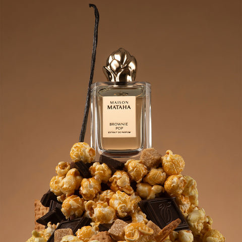 Brownie Pop perfume bottle with golden cap, surrounded by caramel popcorn and chocolate