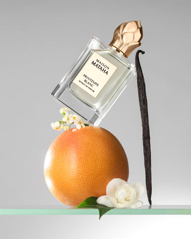Spring Blanc perfume bottle with gold cap, on a citrus and white flower arrangement