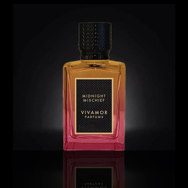 A rectangular bottle of VIVAMOR Parfums with "Midnight Mischief" on the label. This seductive fragrance features a gradient design from amber to pink and a black textured cap, encapsulating the allure of an Extrait de Parfum.