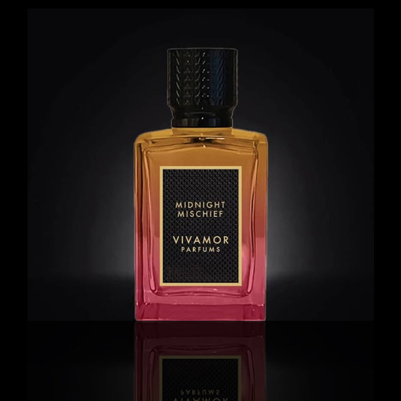 A rectangular bottle of VIVAMOR Parfums with "Midnight Mischief" on the label. This seductive fragrance features a gradient design from amber to pink and a black textured cap, encapsulating the allure of an Extrait de Parfum.