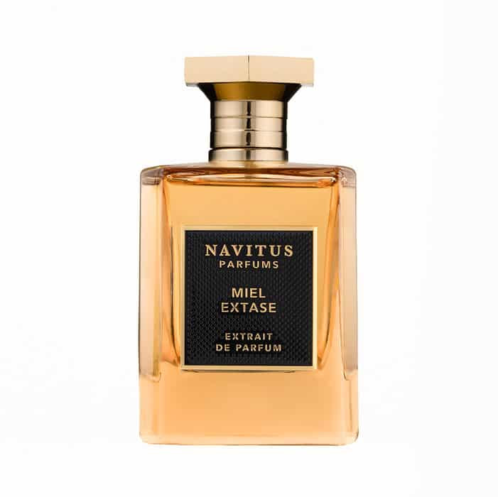 A rectangular glass bottle of Navitus Parfums Miel Extase, crafted by master perfumers Bertrand Duchaufour and Pierre Flores, features a black label and gold cap, containing an amber-colored liquid reminiscent of wild honey.