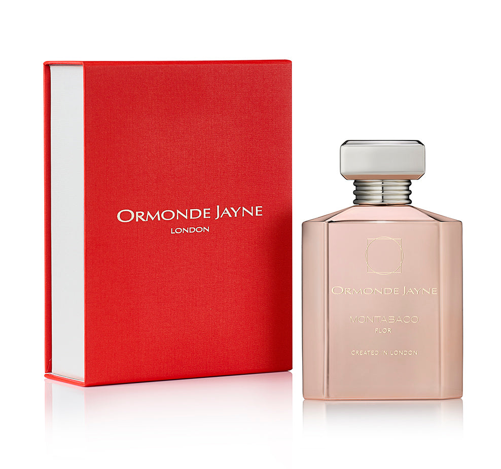 A bottle of Montabaco Flor perfume by Ormonde Jayne displayed in front of a red box. Both the box and bottle feature the Ormonde Jayne logo and text, highlighting this delightful floral perfume with hints of a rose jasmine blend on a sandalwood base.