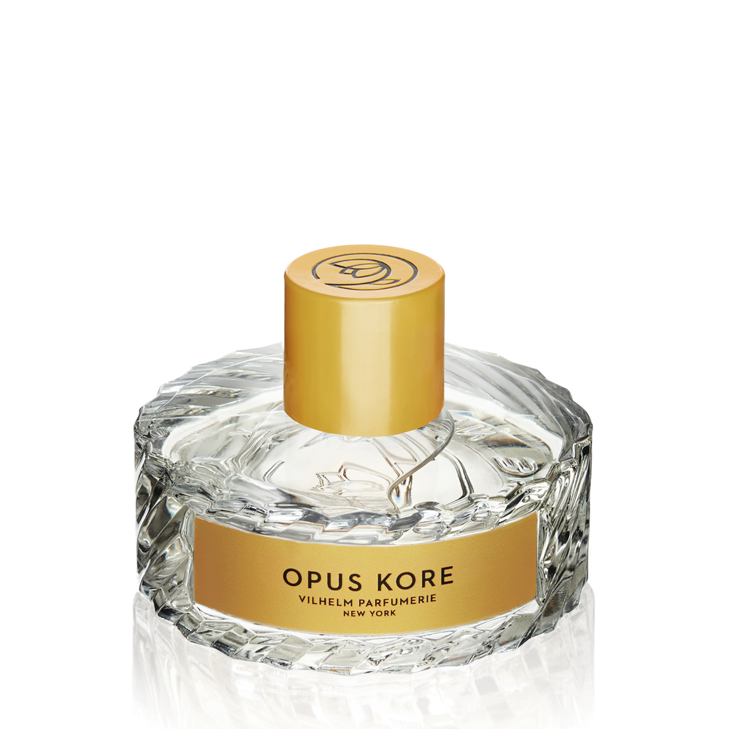 A bottle of Opus Kore by Vilhelm Parfumerie, featuring a textured clear glass bottle with a gold cap and label, on a white background. The fragrance beautifully blends notes of Sicilian lemon and sandalwood for an invigorating and elegant scent.