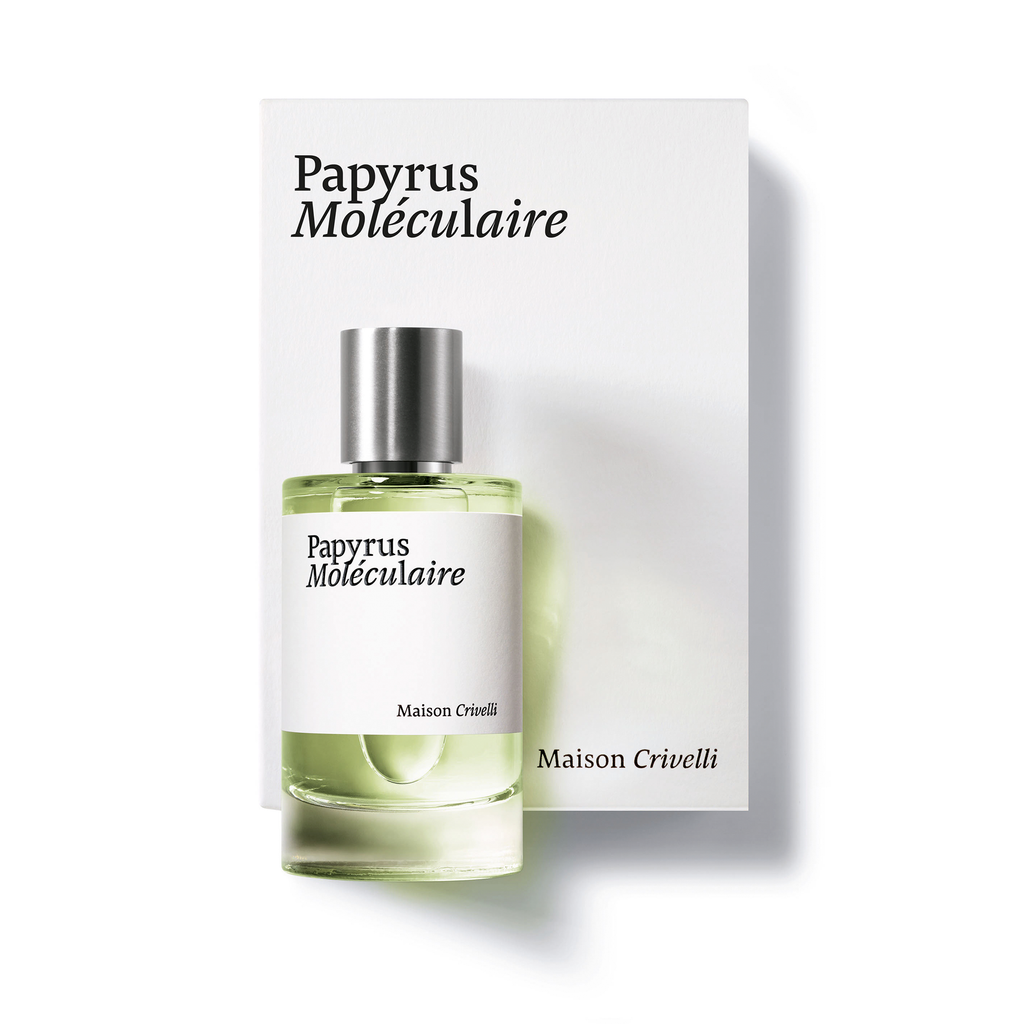 A perfume bottle labeled "Papyrus Moléculaire" from Maison Crivelli stands in front of its elegant white packaging, bearing the same text. The bottle, topped with a silver cap, holds a greenish liquid that suggests the rich essence of papyrus essential oil within this woody, powdery, spicy eau de parfum.