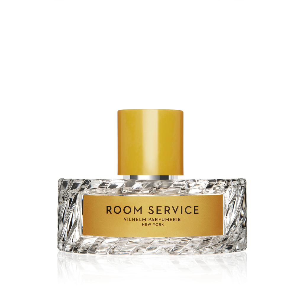 A bottle of Room Service perfume by Vilhelm Parfumerie with a clear, textured glass body and a yellow cap, reminiscent of flower petals. The label on the front reads "ROOM SERVICE" in gold and black text.