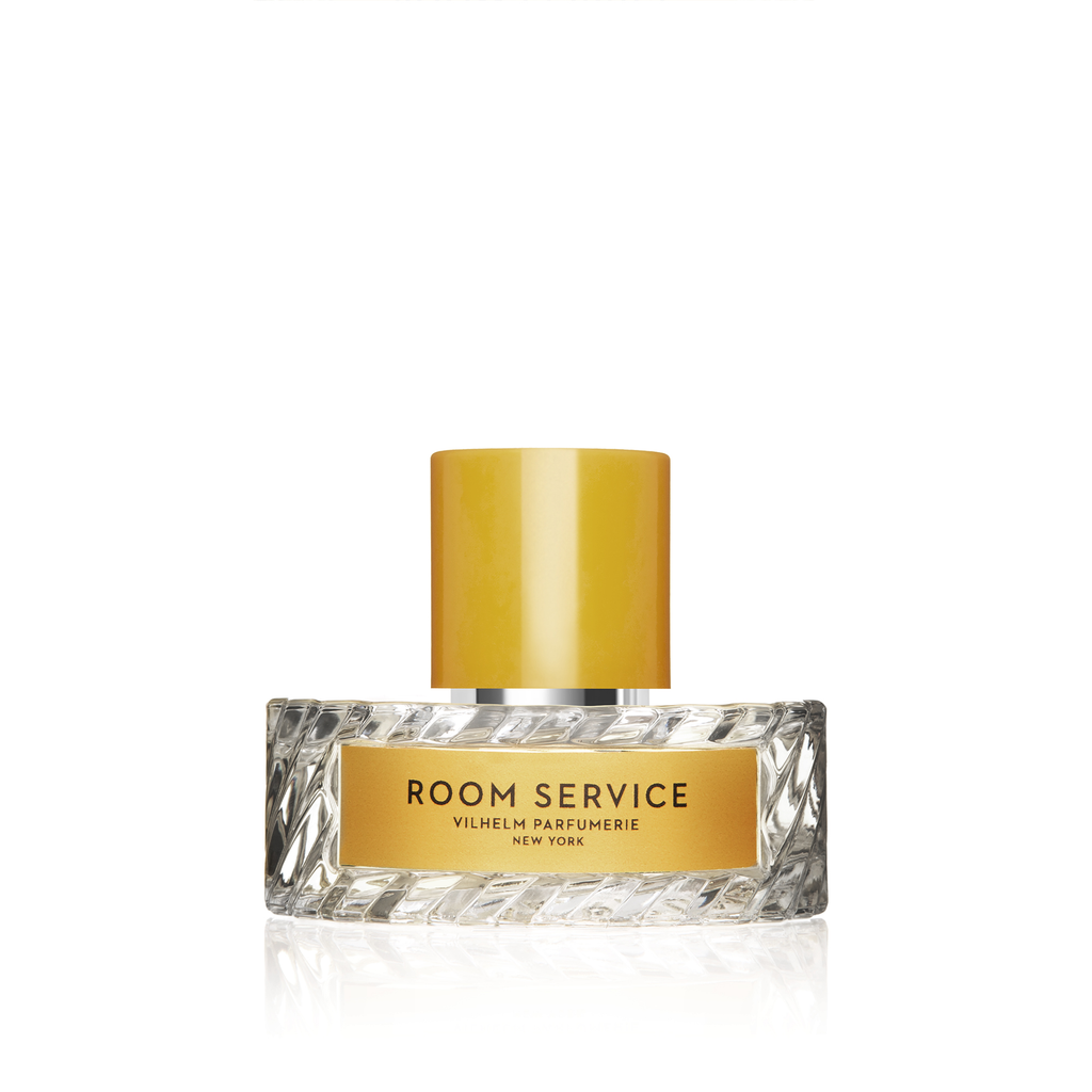 A bottle of Vilhelm Parfumerie's Room Service perfume with a yellow cap and a name label on the front. The textured glass design elegantly mirrors the opulence of a luxury bath.