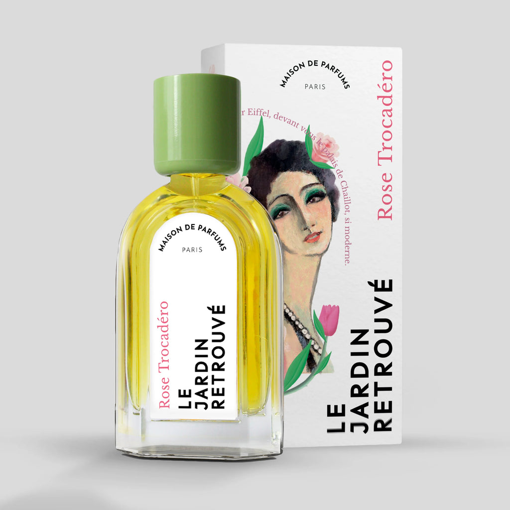 A bottle of Le Jardin Retrouvé Rose Trocadéro Eau de Parfum with a green cap sits elegantly in front of its box, which features an illustrated woman’s face.