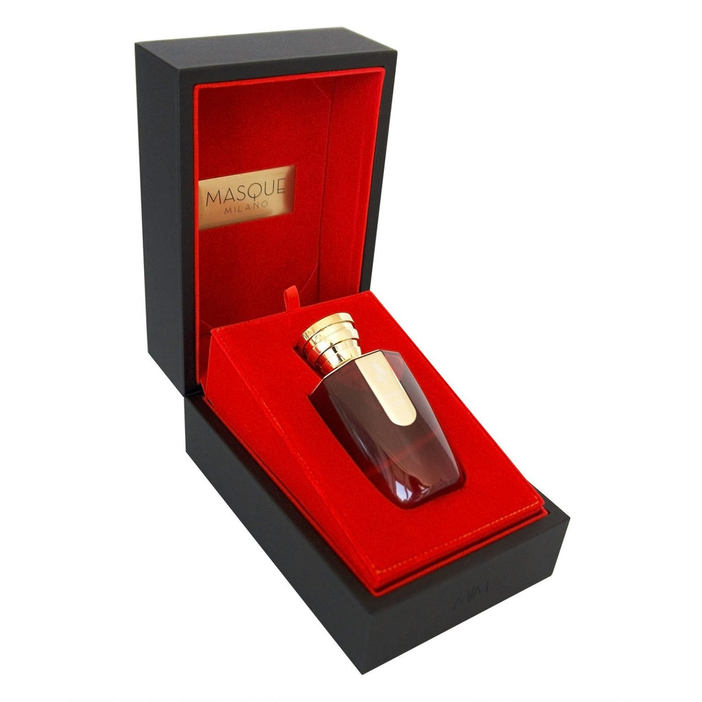 A luxurious "Masque Milano Love Kills Oud" perfume bottle rests in a sleek, dark box lined with red interior. The lid is open to reveal the EDP concentration bottle, securely placed in its fitted compartment.