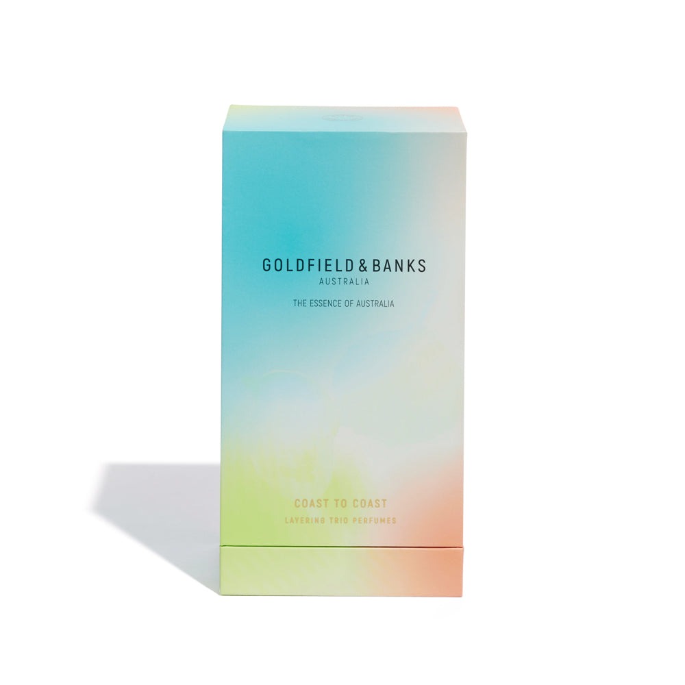 A rectangular box features a gradient color design transitioning from blue to green to peach. The text on the box reads "Goldfield & Banks," "The Essence of Australia," and "Coast to Coast Luxury Travel Trio Perfumes.