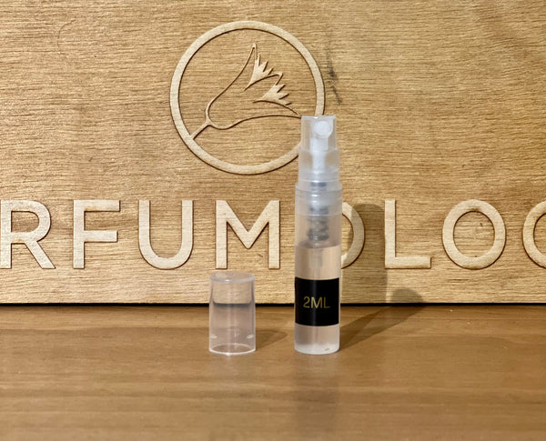 A 2ml spray bottle with a clear cap is placed on a wooden surface in front of a wooden background engraved with the partial text "PERFUMOLOG," evoking the opulence of an Arabian sheikh's realm, as part of 4160Tuesdays' exclusive Crimes of Passion collection, featuring their fragrance "Midnight in The Palace Garden.