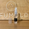 A 2ml perfume spray bottle with a clear plastic cap is placed in front of a wooden background, bearing a bird logo and the partial word "PERFUMOLOGY" engraved, exuding an inviting floral fragrance. The product is You or Someone Like You by État Libre d'Orange.