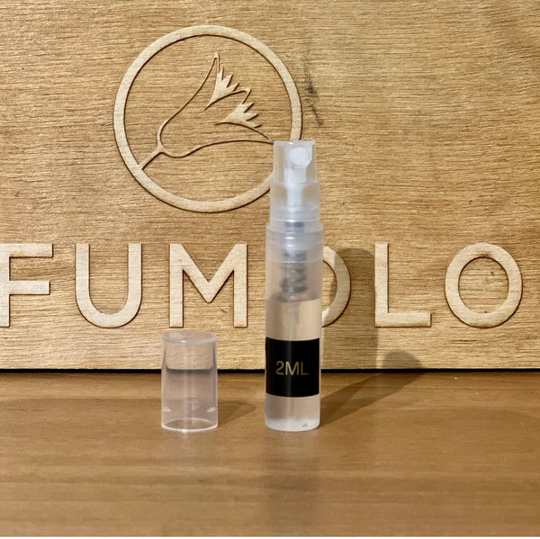 A small 2ml spray bottle with a transparent cap is placed in front of a wooden background that has an engraved bird logo and partial text visible, reminiscent of a quaint chocolate shop. The product is called "Over the Chocolate Shop" by 4160Tuesdays.