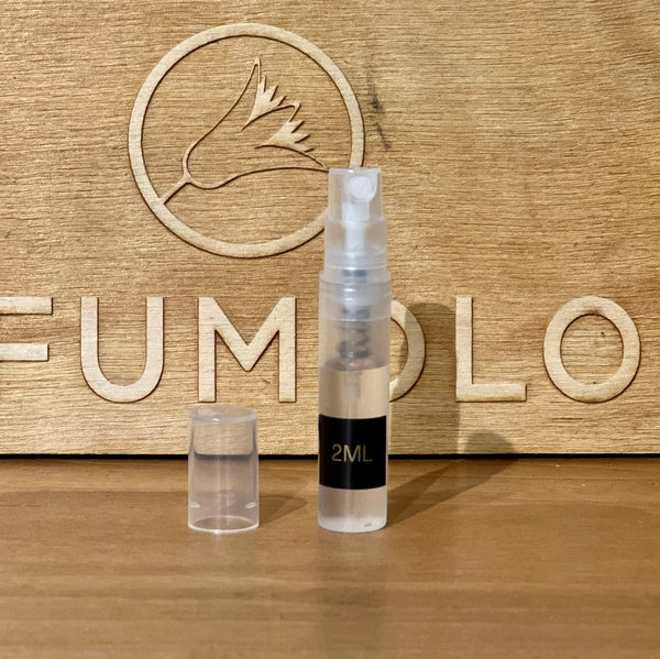 A 2ml clear spray bottle with a black label is placed in front of a wood background featuring an engraved bird logo and partial text saying "Zoologist." The bottle cap is beside the bottle, hinting at the delightful blend of fruity nectars and floral tones inside.