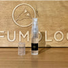 Perfume spray bottle with small vial on wooden display with gold emblem