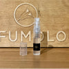 A small clear spray bottle with "2ML" written on it stands on a wooden surface in front of a background featuring engraved letters and the Zoologist bird logo. The bottle's cap is placed beside it, hinting at the fragrance within—possibly laced with ambergris from the elusive Zoologist Squid perfume line.