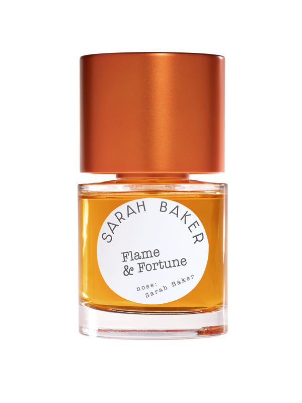 A bottle of "Flame & Fortune" perfume by Sarah Baker, featuring an amber liquid inside, a bronze cap, and a subtle hint of tuberose essence.