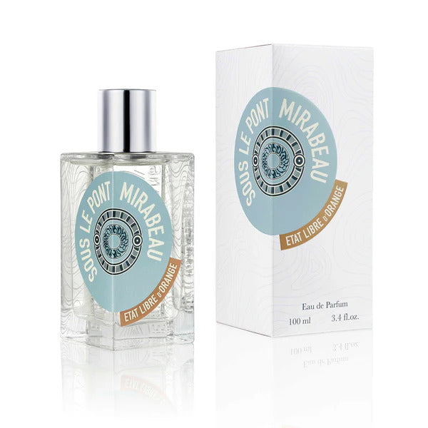 A clear glass bottle of "SOUS LE PONT MIRABEAU" Eau de Parfum by État Libre d'Orange sits next to its matching rectangular white box adorned with blue and brown design accents and text, subtly hinting at the alluring notes of sandalwood.