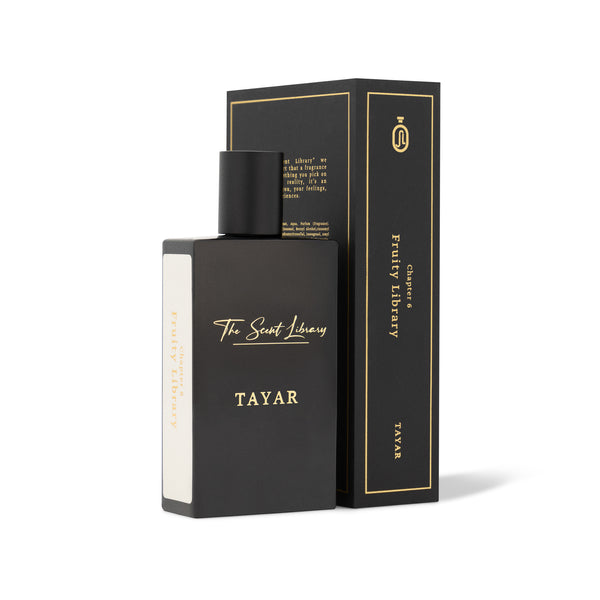 A black perfume bottle labeled "The Scent Library - Tayar" is placed next to its matching black box, both with gold text accents, promising an olfactory journey.