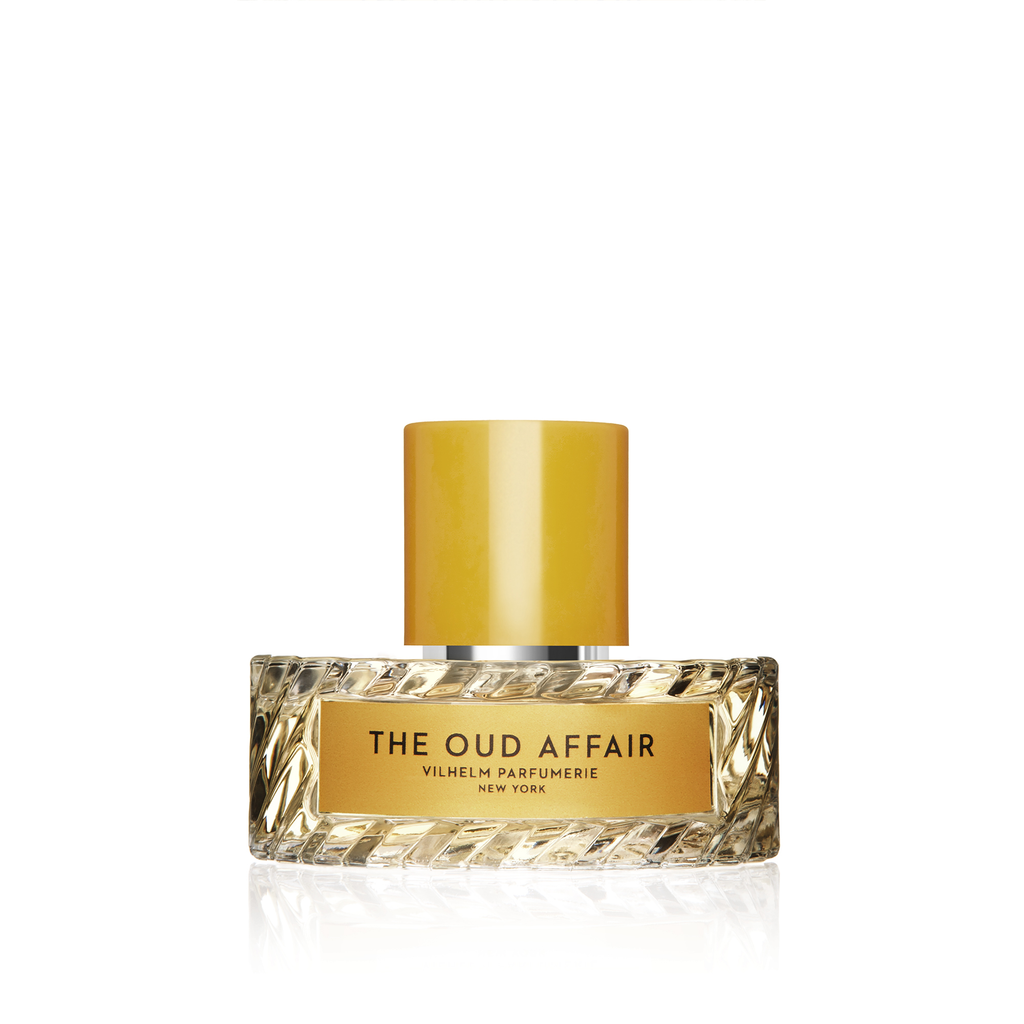 A glass bottle of "The Oud Affair" perfume by Vilhelm Parfumerie, featuring a yellow-gold cap and a gold label, infused with hints of wild honey.
