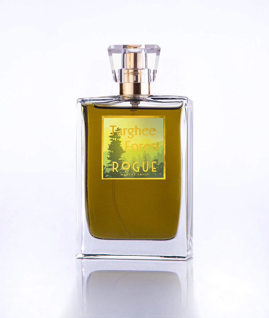 A clear glass perfume bottle with a gold and green label reading "Targhee Forest, Rogue Perfumery." The perfume inside is a greenish liquid, evoking woody notes of pine and cedar. The bottle has a geometric, transparent cap.