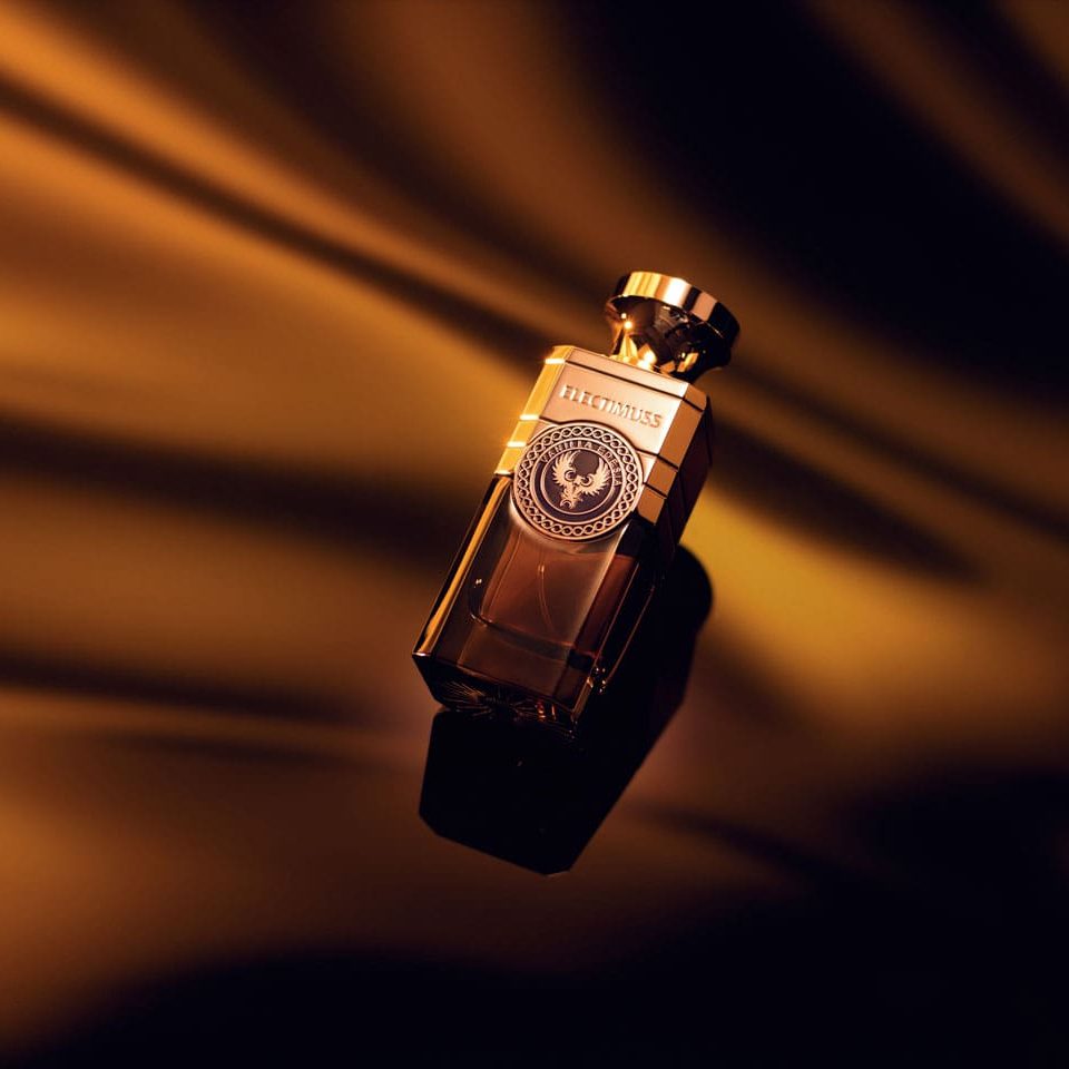 A gold-colored perfume bottle of the luxurious Vanilla Edesia by Electimuss rests on a reflective surface against a swirling, golden backdrop.